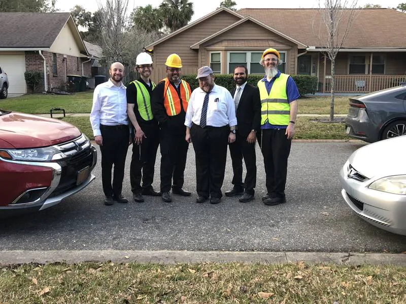Six community members, some in hard hats and safety vests, standing together on a residential street in Jacksonville